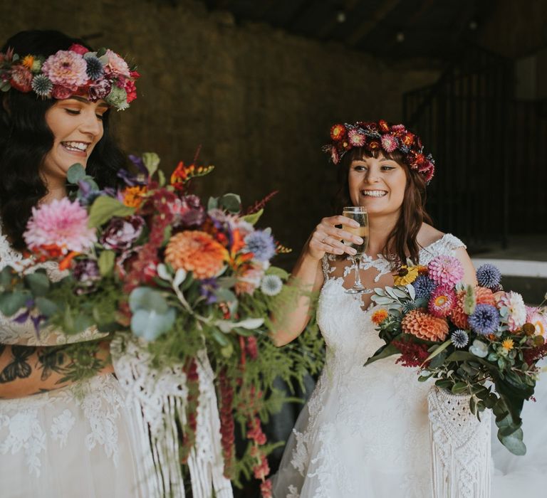 Two Brides in Lace Wedding Dresses with Colourful Flower Crowns and Bouquets at the Drinks Reception