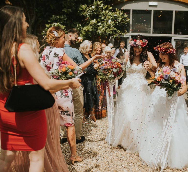 Confetti Moment with Two Brides in Lace Wedding Dress and Colourful Flower Crowns