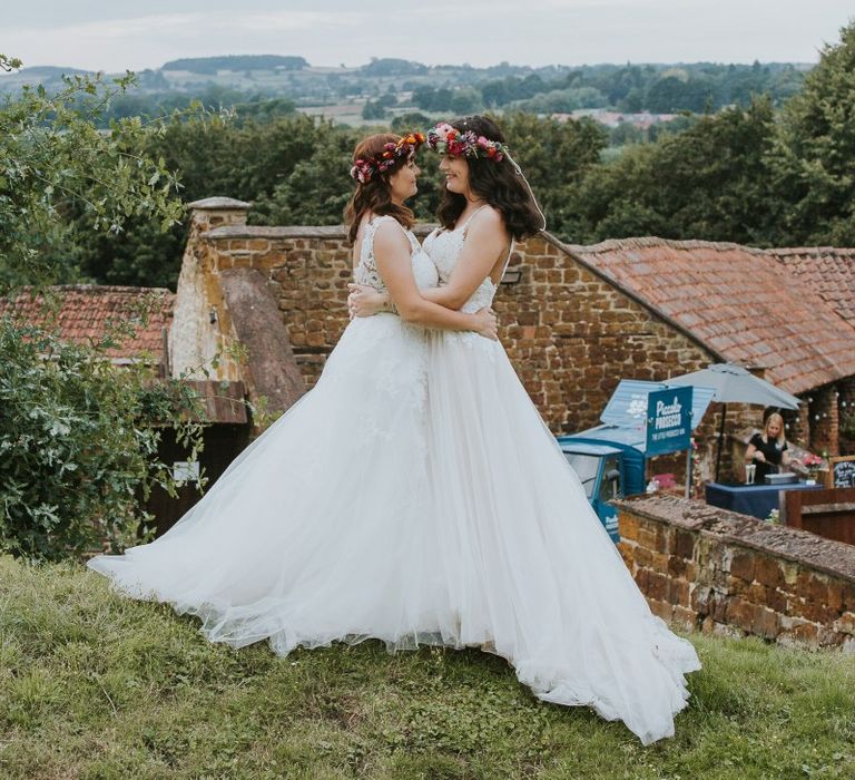 Two Brides Embracing in Lace and Tulle Wedding Dresses and Flower Crowns