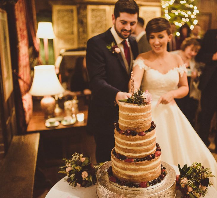 Bride &amp; Groom Cutting the Naked Wedding Cake | Burgundy &amp; Gold Winter Wedding at Ramster Hall Weddings, Surrey | Matt Penberthy Photography | John Harris Wedding Films