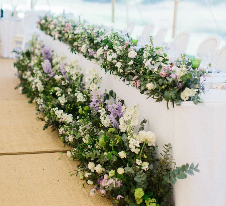 White, green and lilac flowers from the Church moved to reception to dress top table | Papakata Sperry Tent Wedding at family home | Sassi Holford Dress with added ivory Ostrich feathers to veil | Manolo Blahnik shoes | Images by Melissa Beattie