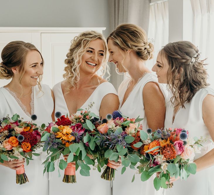 Bridesmaids in white jumpsuits with bright wedding flowers