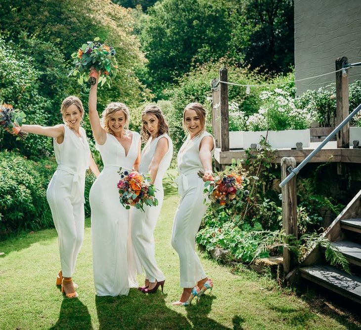 White jumpsuits for bridesmaids with bright wedding flowers