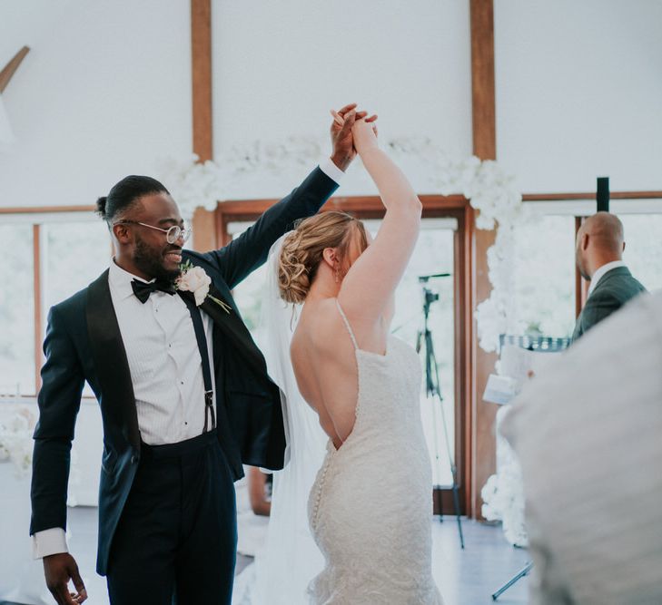 Groom in tuxedo twirling his bride in Morilee wedding dress