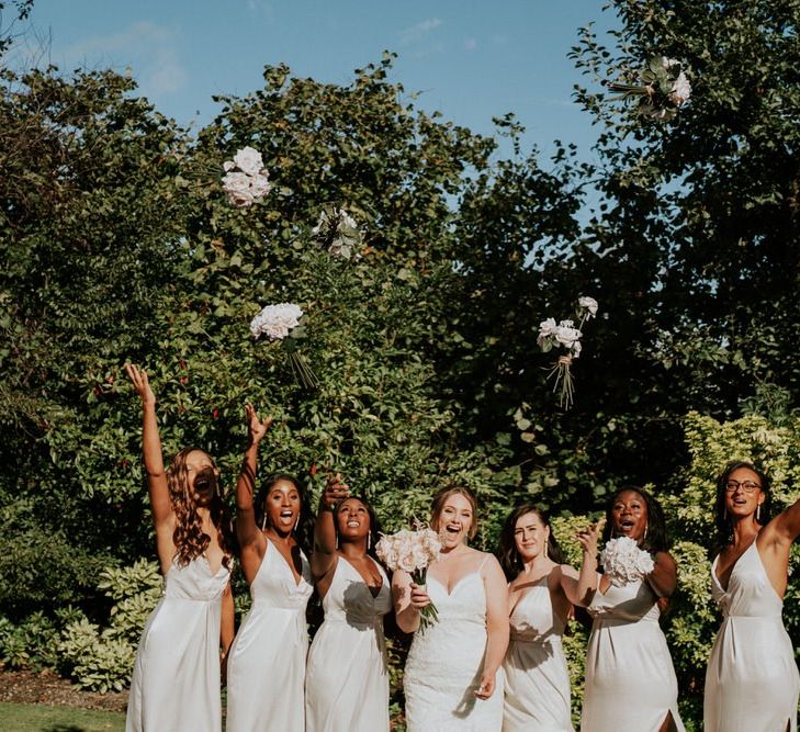 Bridesmaids in white dresses throwing their bouquets in the air