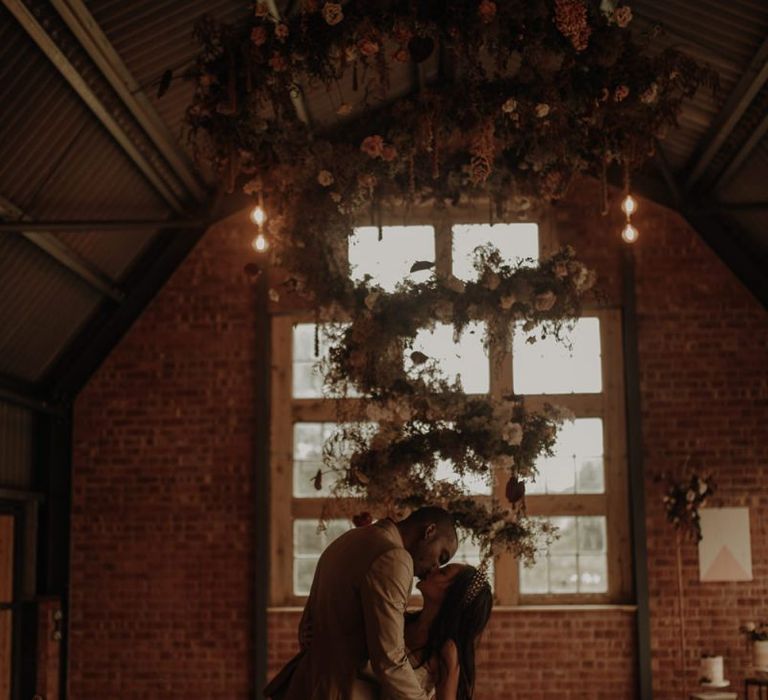 Bride and groom kissing under a floral spiral installation