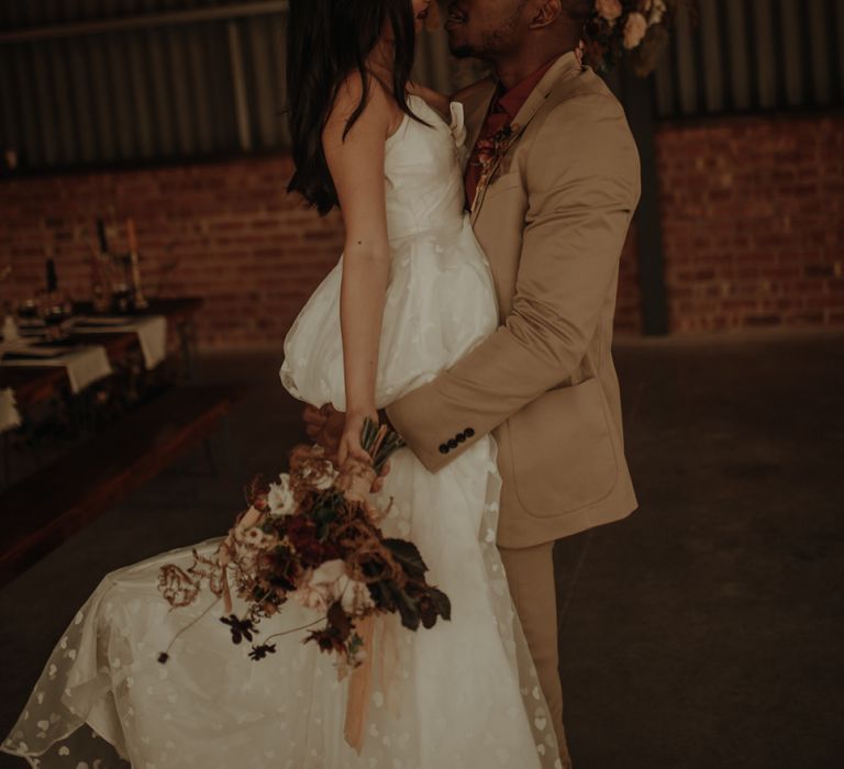 Groom in beige siut picking up his bride in a embroidered wedding dress