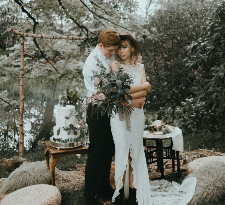 Groom Embracing His Boho Bride in Lace Wedding Dress with Front Split, Boots and Felt Hat