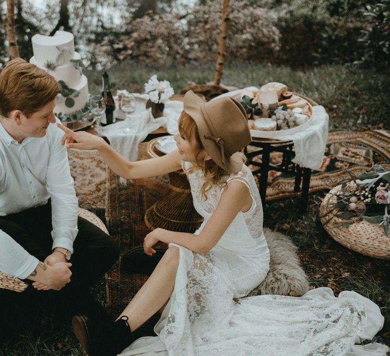 Boho Bride in Lace Wedding Dress and Felt Hat and Groom in White Shirt Enjoying Their Grazing Table