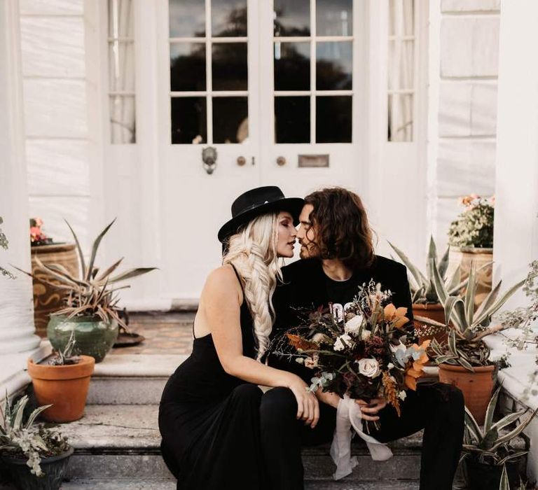 Groom in black velvet blazer holding a autumn wedding bouquet at Preston Court