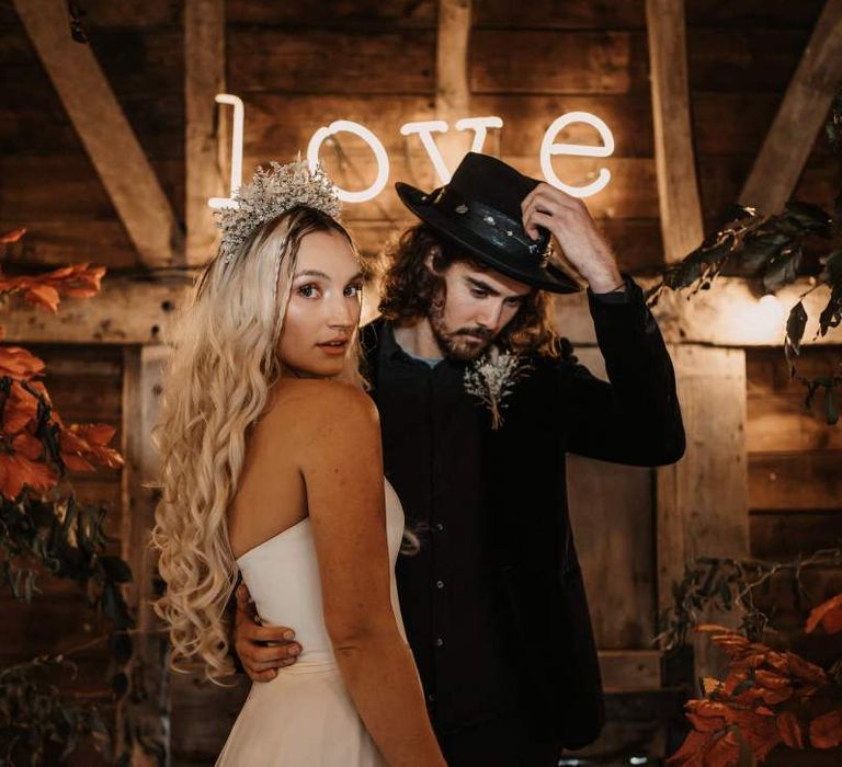 Stylish bride and groom standing in front of a LOVE neon sign