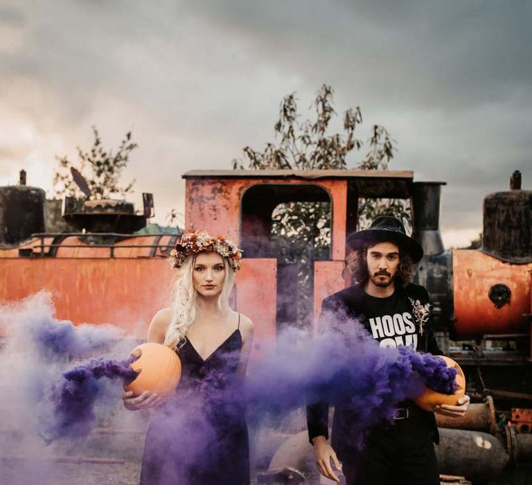 Stylish bride and groom with purple smoke bombs at Halloween wedding