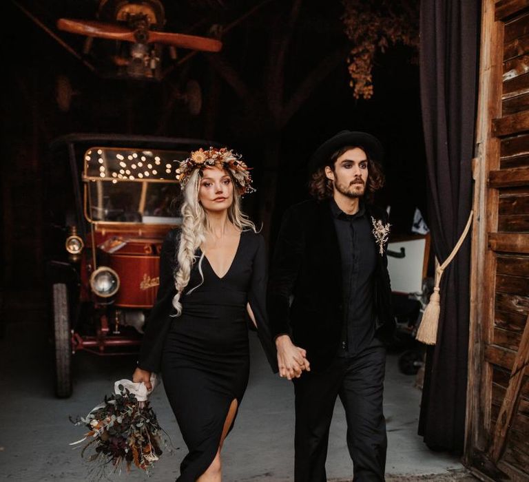 Bride in black dress with side braid and flower crown holding her grooms hand in a black shirt and hat for Halloween wedding