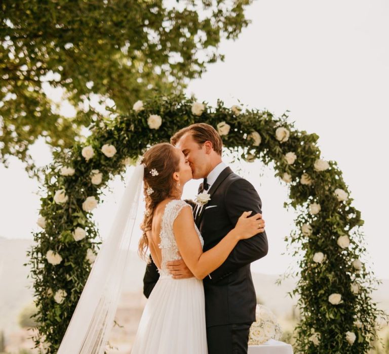 Bride in Bespoke Wedding Dress and Groom in Tuxedo Kissing at the Wedding Ceremony