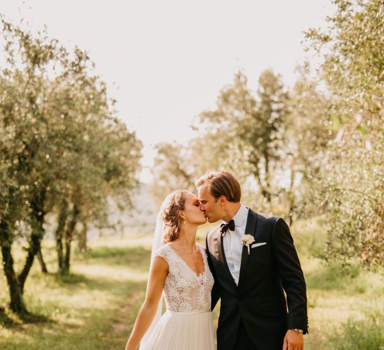 Bride in Bespoke Wedding Dress with Lace Bodice and Groom in Tuxedo Kissing