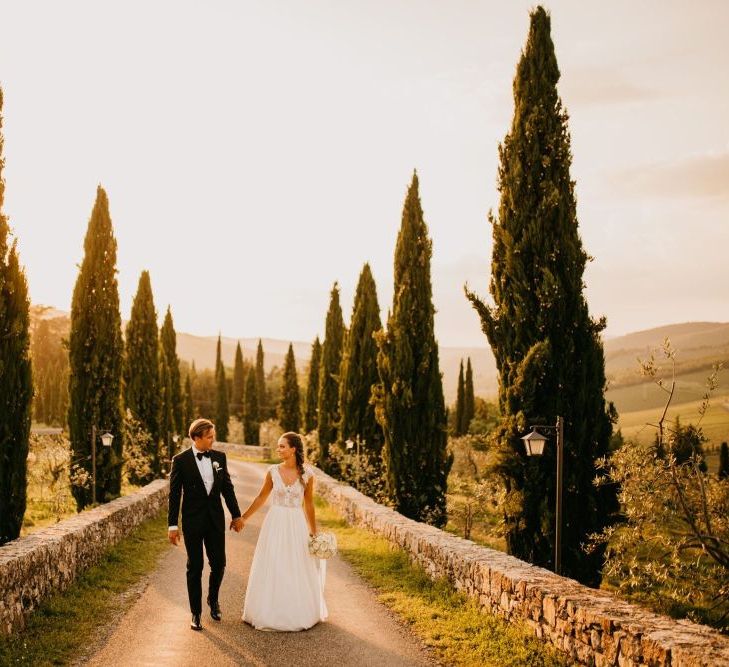 Golden Hour Portrait with Bride in Bespoke Wedding Dress and Groom in Tuxedo and Bow Tie Holding Hands