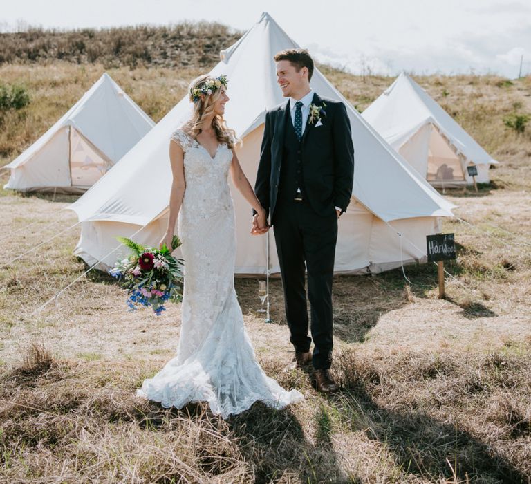 Bride in Lace Watters Wedding Dress and Groom in Hugo Boss Suit Standing in their Glamping Field