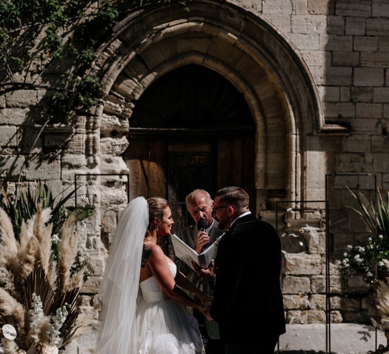 Bride in Feather Wedding Dress and Groom in a Tuxedo Exchanging Vows at the Altar