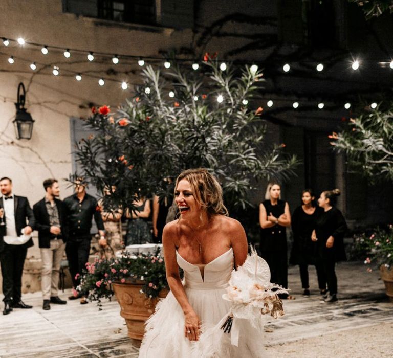 Happy Bride in Off the Shoulder Bodice and Feather Skirt About to Toss Her Wedding Bouquet