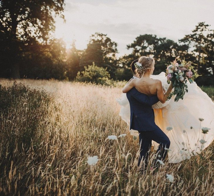 Groom Carries Bride Through Field For Summer Wedding