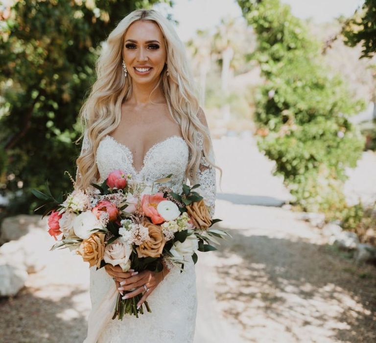 Bride walking down the aisle in a lace wedding dress holding a coral bouquet