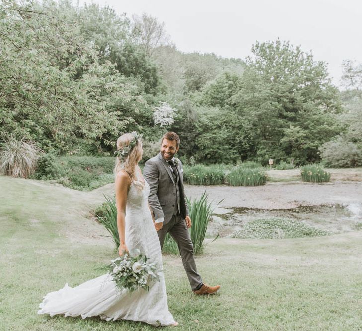 Bride in Lace Wedding Dress and Flowers Crown and Groom in Brown Wool Suit Walking Hand in Hand