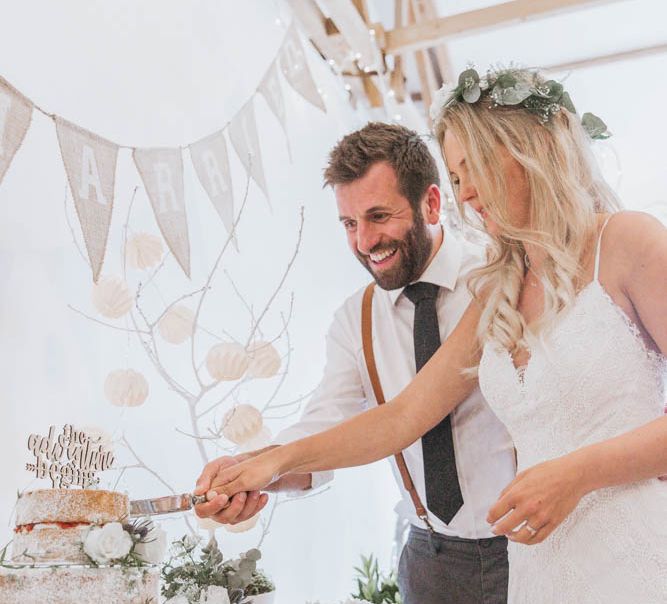 Boho Bride in Lace Wedding Dress and Flower Crown and Groom in Braces Cutting the Homemade Naked Wedding Cake