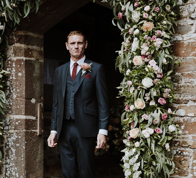 Groom in Three-piece Clifton Suit Standing Next to a Church Floral Arch