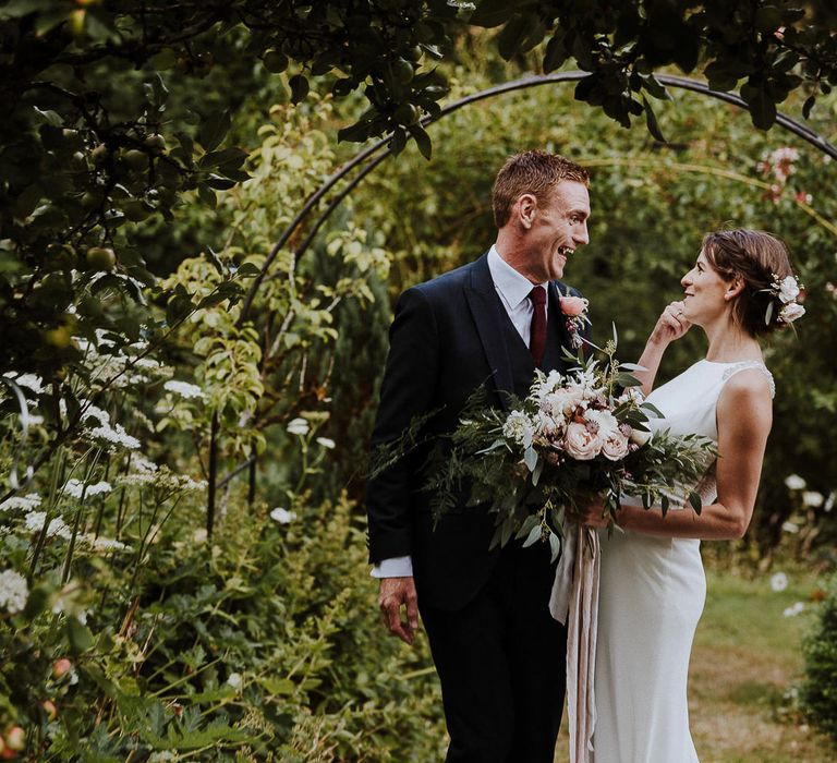 Bride in High Neck Mikaella Bridal Fitted Wedding Dress and Groom in  Clifton Suit Laughing