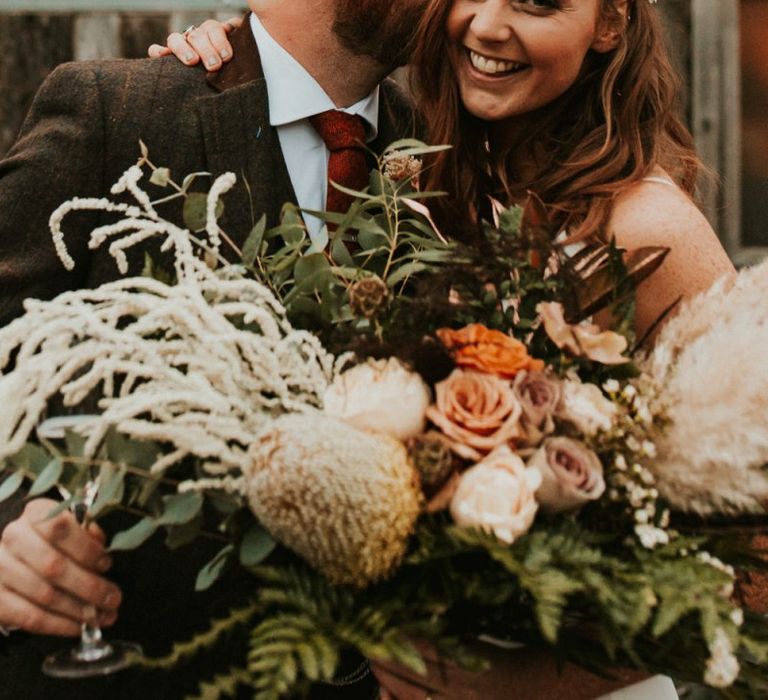 Bride and groom at Winter wedding with large bouquet with bridesmaid jumpsuit