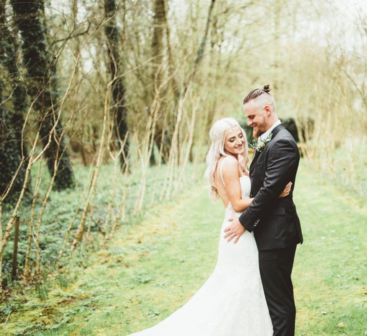 Bride in Danni Made With Love Bridal Wedding Dress and Groom in Reiss Suit Cuddling in the Countryside