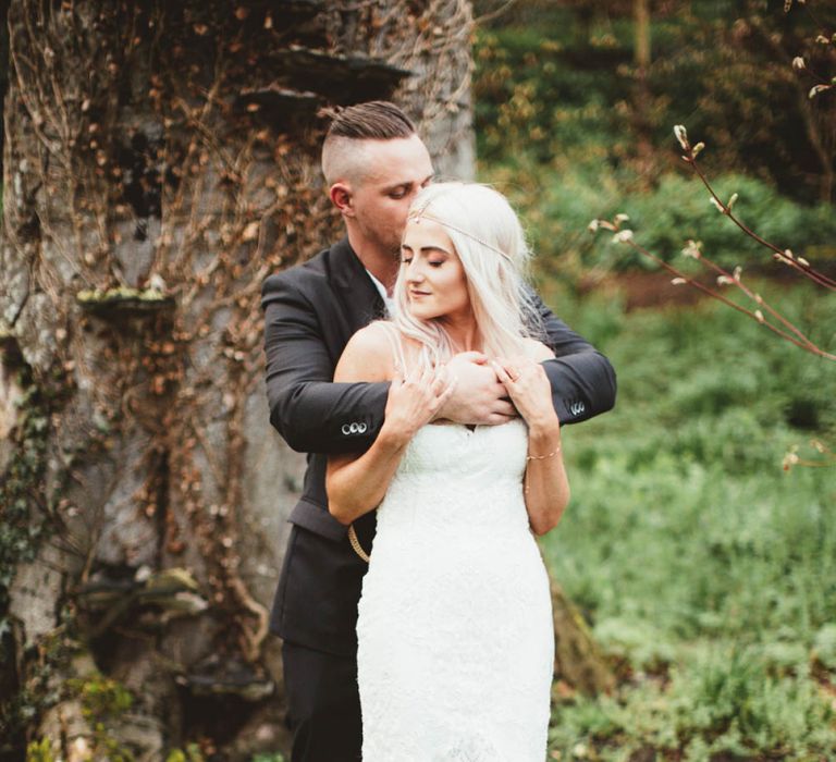 Bride in Danni Made With Love Bridal Wedding Dress and Groom in Reiss Suit Embracing in the Woodland