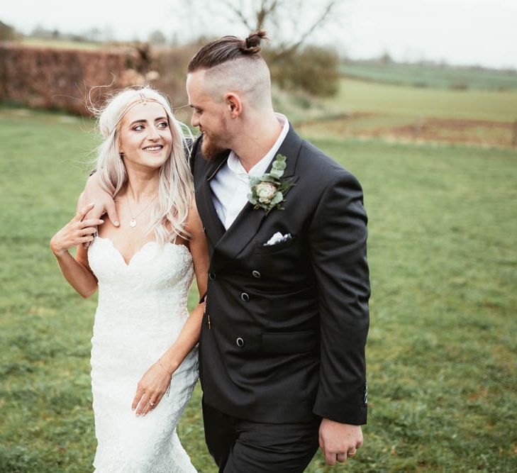 Bride in Danni Made With Love Bridal Wedding Dress and Groom in Reiss Suit Arm in Arm in the Field