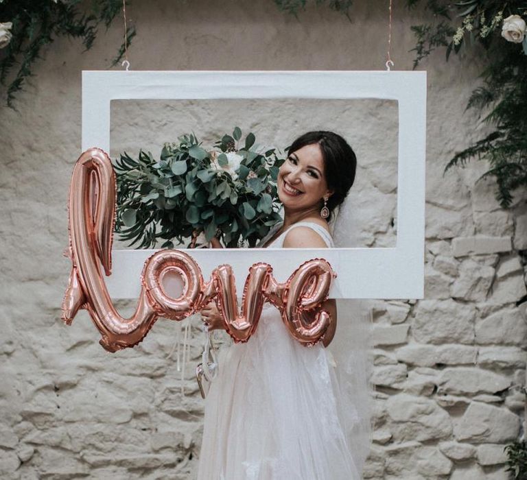 Bride posing at Selfie station with foil ballon and white frame