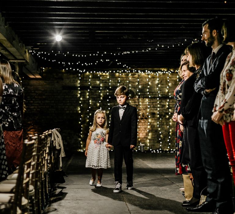 Page Boy and Flower Girl Walking down the Aisle with Fairy Light Wedding Decor