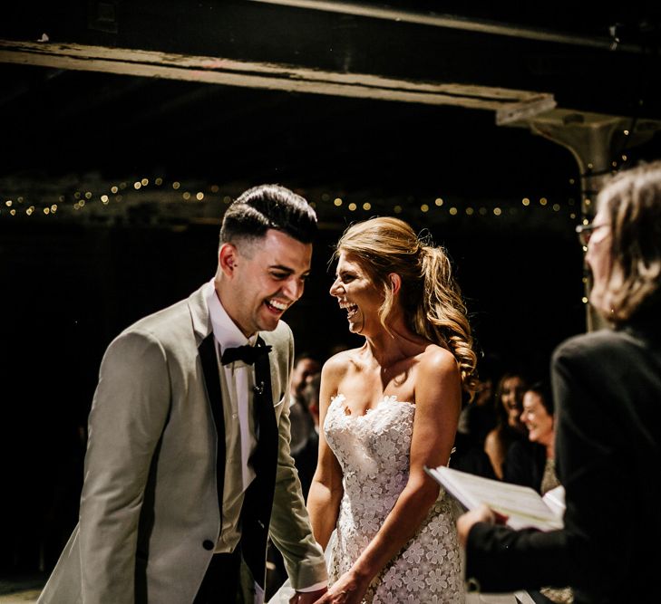 Bride in Lace Tara Keely Wedding Dress and Groom in Grey Tuxedo Jacket Laughing at the Altar