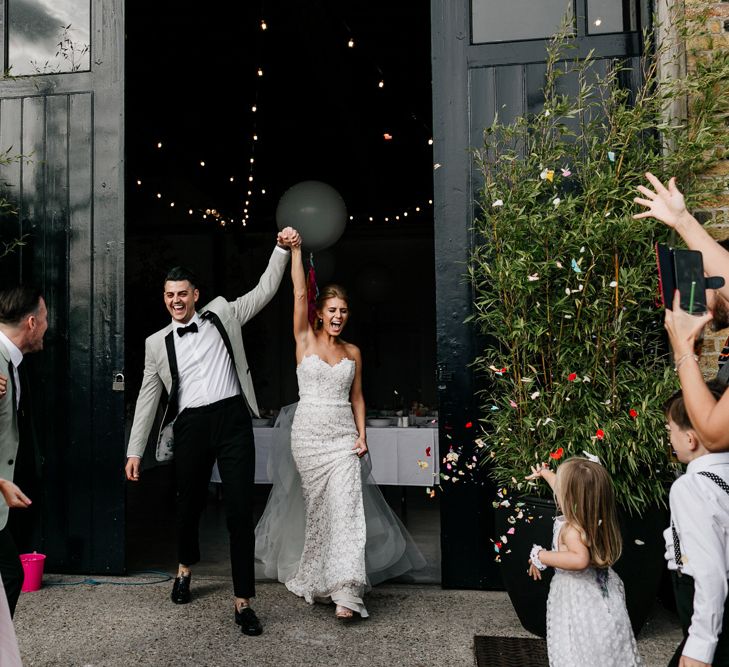 Bride in Tara Keely Wedding Dress and Groom in Grey Tuxedo Jacket Exiting Wedding Venue Hand in Hand