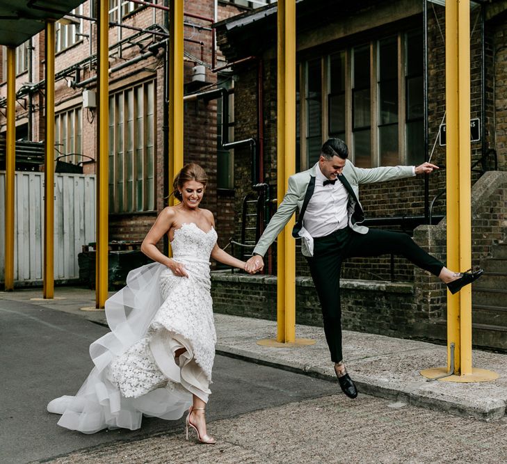 Bride in Tara Keely Applique Wedding Dress and Groom in Grey Tuxedo Jacket Jumping for Joy