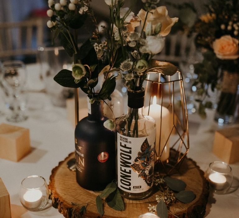 Rustic centrepiece decor with tree slice, fairy lights, gin bottles and flower stems