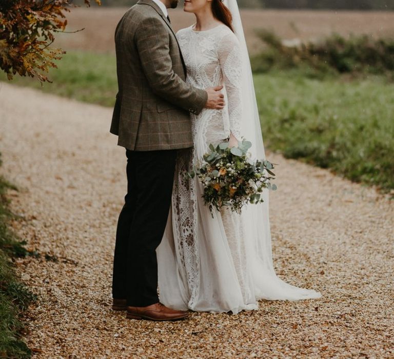 Groom in wool blazer embracing his bride in Grace Loves Lace wedding dress