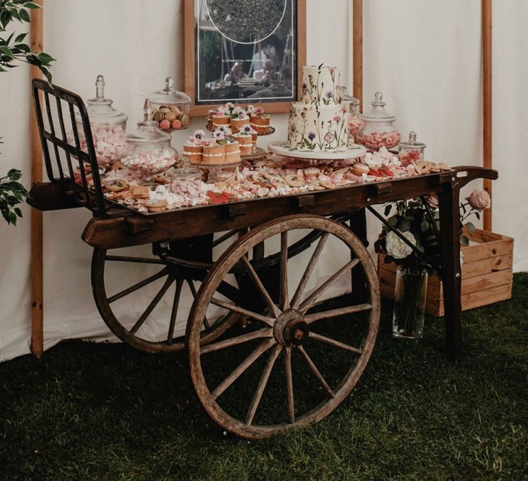 Delicious cake cart at marquee wedding with cupcakes and pressed flower wedding cake