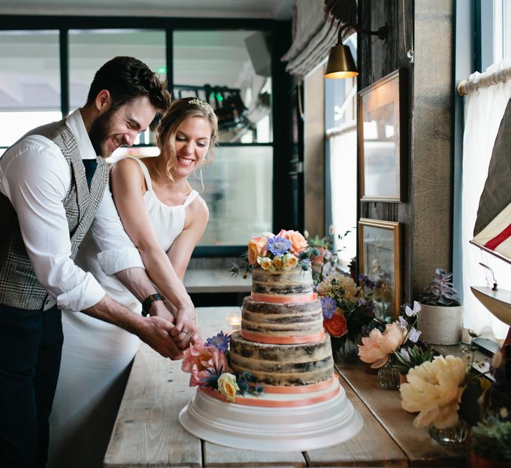 Bride and Groom Cutting the Semi Naked Wedding Cake Decorated with Ribbon and Flowers