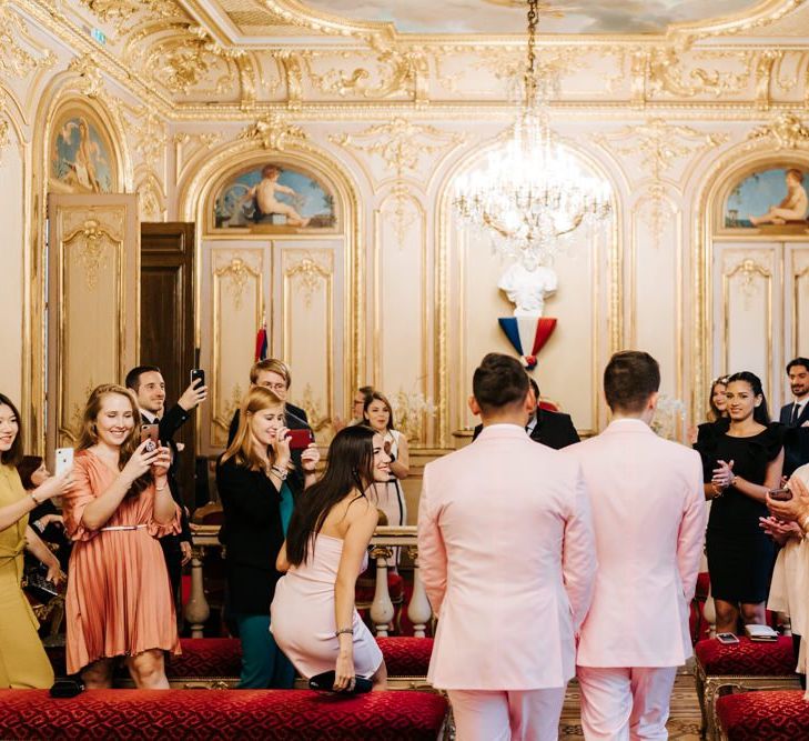 Grooms wearing pink wedding suits walk down the aisle together at beautiful ceremony in Paris city hall