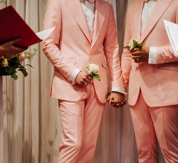 Grooms holding hands as two of their closest friends officiate the second ceremony