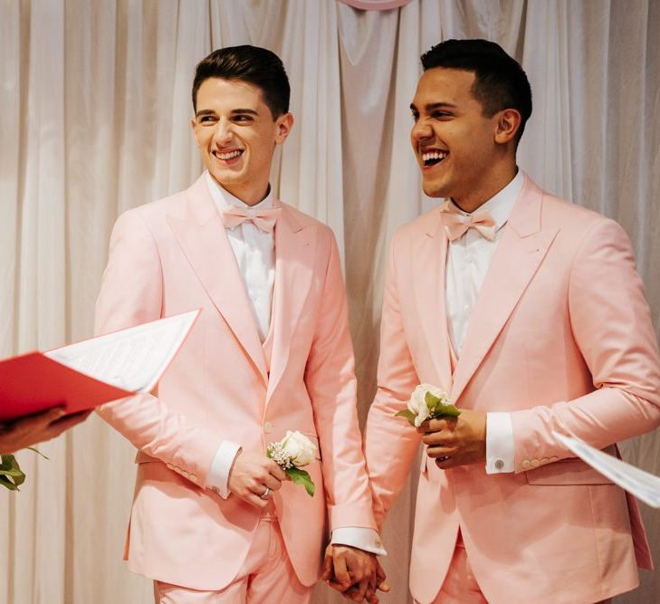 Grooms holding hands as two of their closest friends officiate the second ceremony