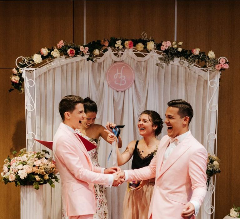 Both grooms wearing pink wedding suits and their best friends smile at Paris same sex wedding