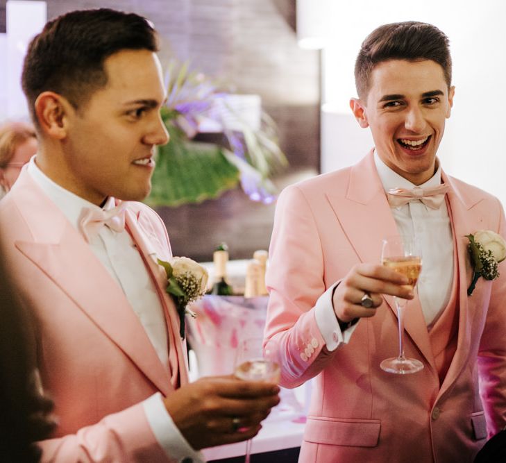 Grooms wearing pink wedding suits toast with champagne and smiling faces at same-sex Paris reception