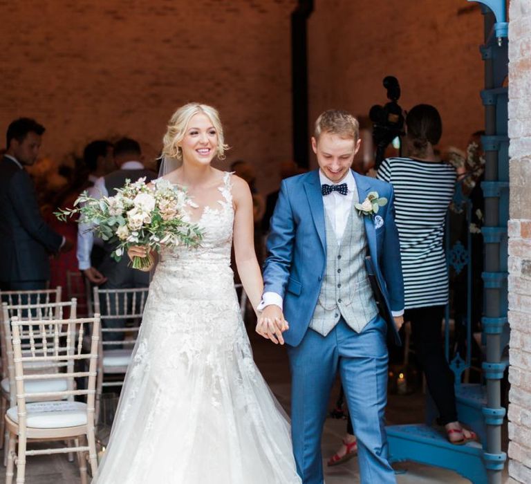 Bride in Lace Pronovias Wedding Dress and Groom in Navy Suit Holding Hands Exiting the Wedding Ceremony