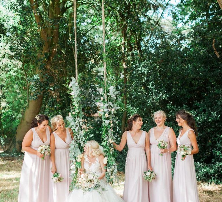 Bridal Party Portrait with Bride in Pronovias Wedding Dress Sitting on a Swing and Bridesmaids in Pink Maids to Measure Dresses