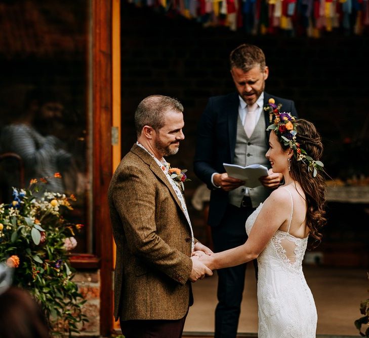 Bride in Lace Sottero &amp; Midgley Wedding Dress and Groom in Wool Blazer Holding Hands During the Wedding Ceremony